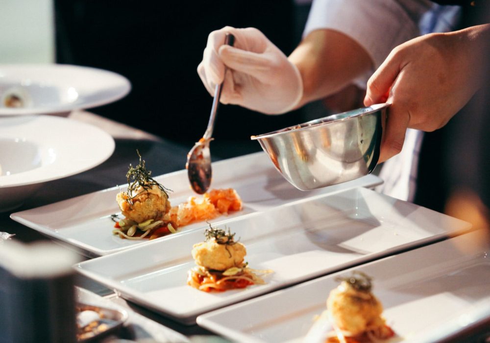 Un cuoco impiatta con cura dei piatti gourmet su un vassoio rettangolare. Un cuoco impiatta con cura dei piatti gourmet su un vassoio rettangolare.